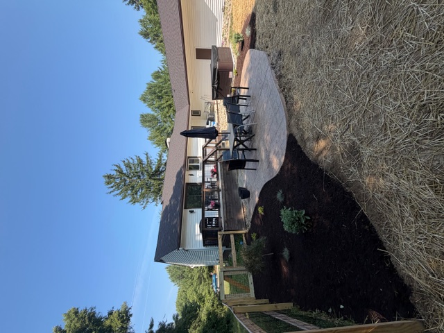 Finished backyard patio area with mulch beds, plantings, and straw-covered lawn area